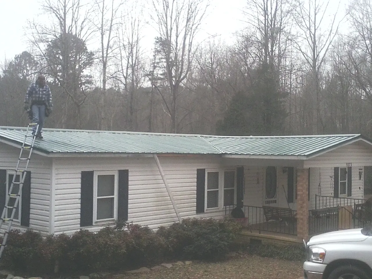 Worker on a ladder beside a new green metal roof on a ranch home in Kalamazoo