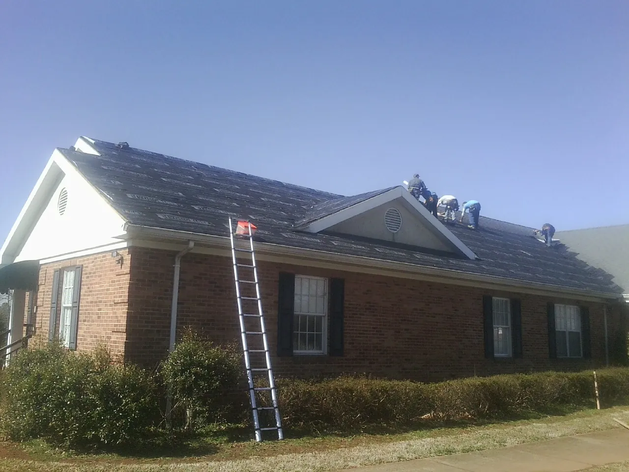 Crew tearing shingles off a brick ranch roof with a ladder set — Emergency Roof Repair work by our crew in Kalamazoo