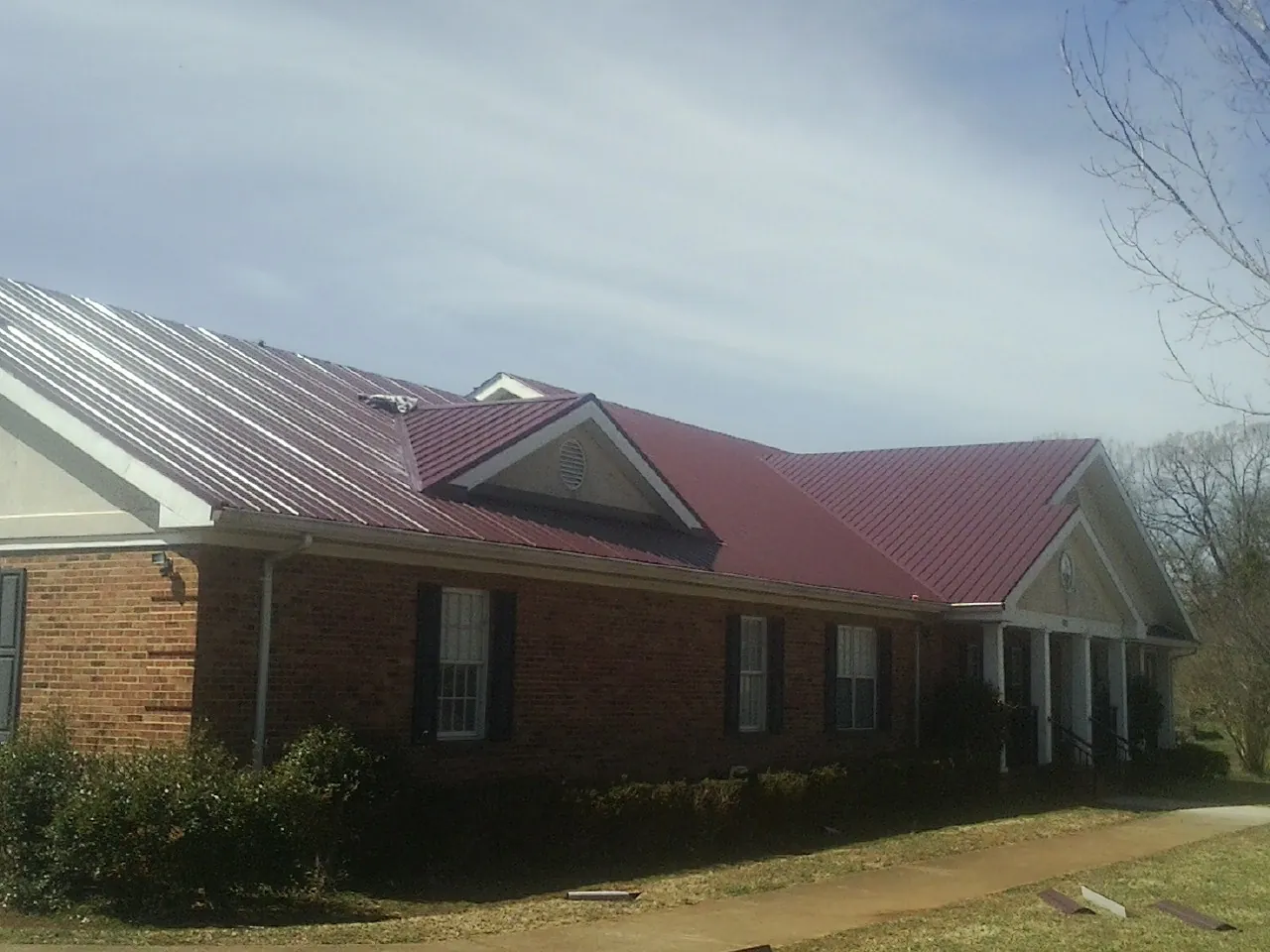 Red metal roof with gabled entries on a long brick building, from a Hail Damage Roof Repair job in Kalamazoo
