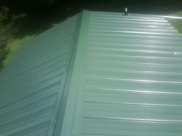 New green metal panels meeting at the ridge of a roof — Flat Roof Repair work by our crew in Kalamazoo