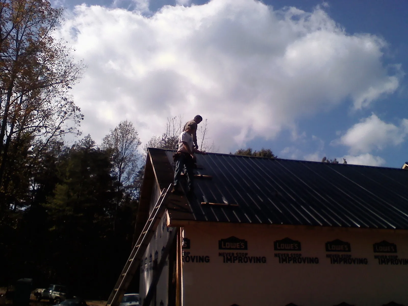 Roofer fastening dark metal panels high against a cloudy sky, from a Roof Inspection job in Kalamazoo