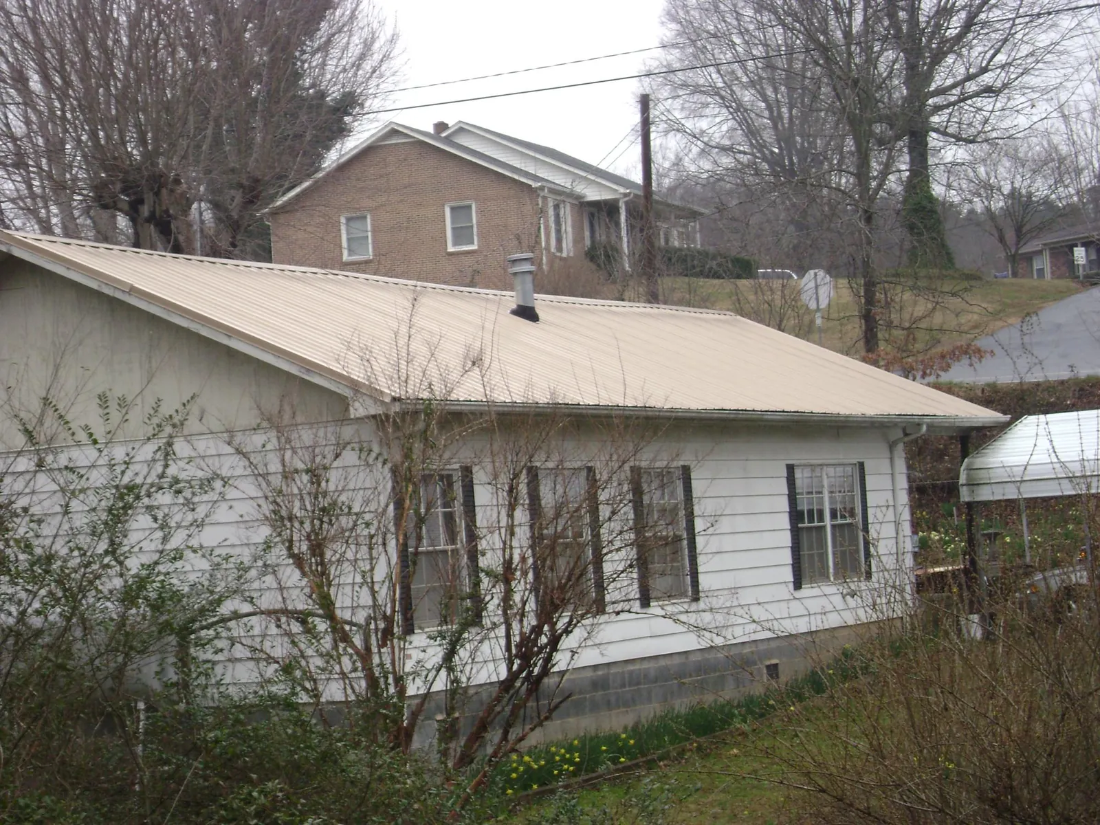 Tan metal roof on a white sided house set into a hillside — Commercial Roofing by Roofing Brothers in Kalamazoo